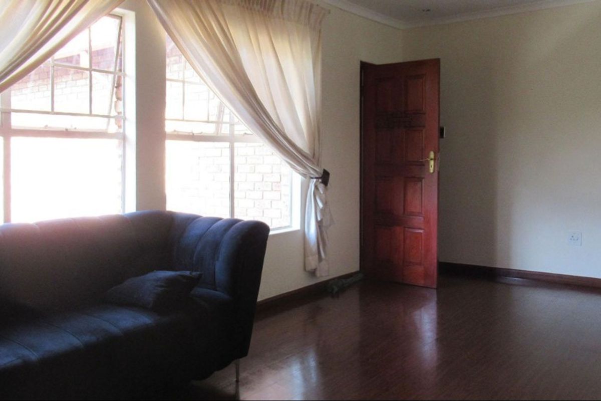 A living room featuring dark laminate flooring, a timber door, and natural light from large windows.