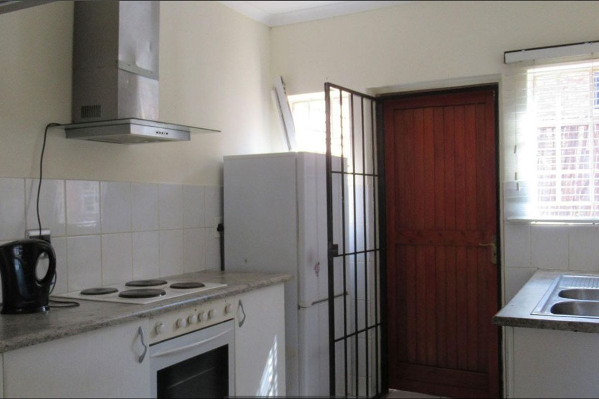 Functional kitchen featuring a built-in oven, electric hob, stainless steel extractor fan, double bowl sink, and direct access to an exterior door with security gate.