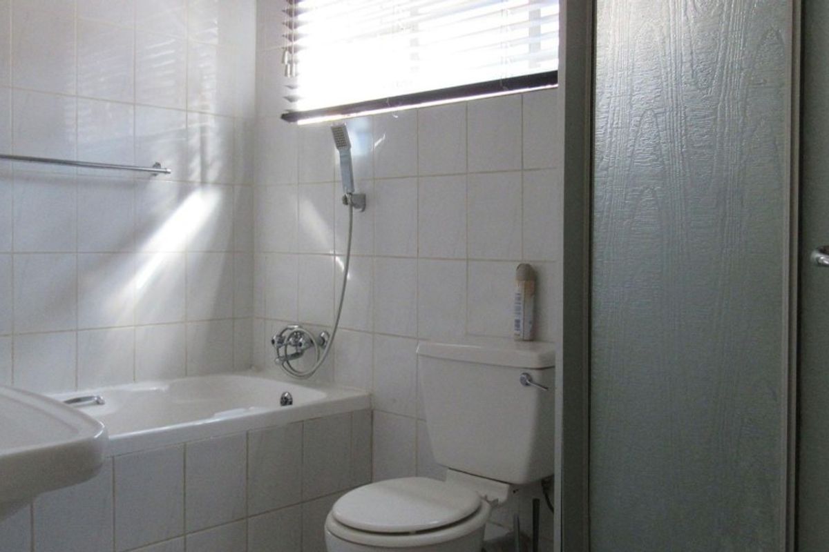 A functional bathroom featuring a built-in bathtub with shower attachment, pedestal washbasin, and toilet, finished with white ceramic wall tiles.