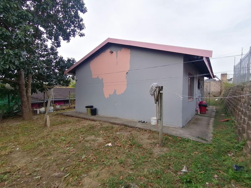 Rear view of the property showing the exterior wall with significant paint peeling and exposed plaster, set against a garden area with a retaining wall.
