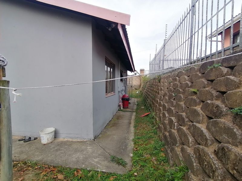 Side exterior view showing a concrete pathway, a stone retaining wall, and perimeter electric fencing.