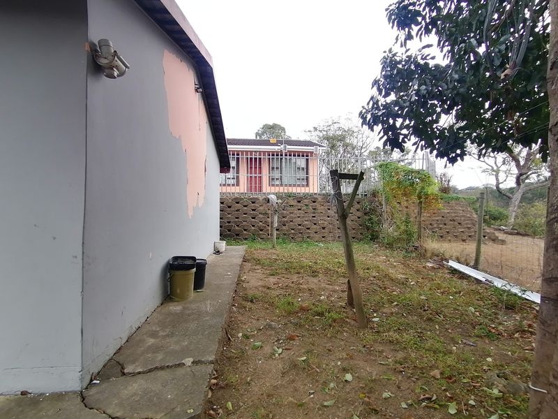 Rear exterior view showing a concrete pathway, retaining wall, and security fencing with visible wear to the exterior wall finish.