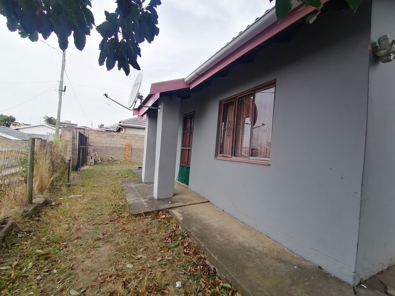Rear exterior view of the house featuring a concrete walkway, security bars on windows, and a perimeter wall in a modest garden setting.