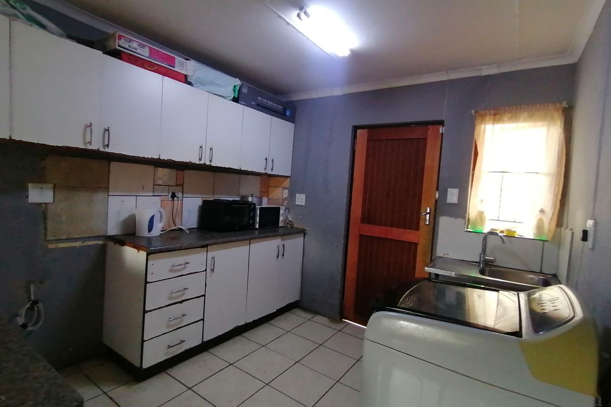 A functional kitchen featuring built-in cabinetry, tiled flooring, and a stainless steel sink, offering potential for cosmetic updates and modernization.