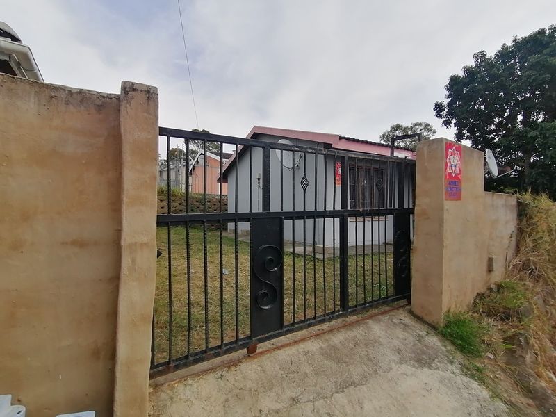 Front view of the property featuring a metal security gate, concrete boundary wall, and a small front yard area.