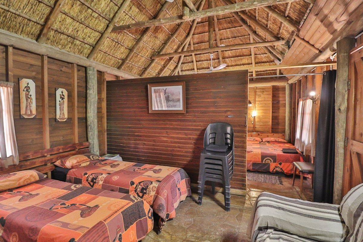 Rustic bedroom featuring a traditional thatched roof, exposed timber beams, wood-paneled walls, and durable stone flooring in a farm-style setting.