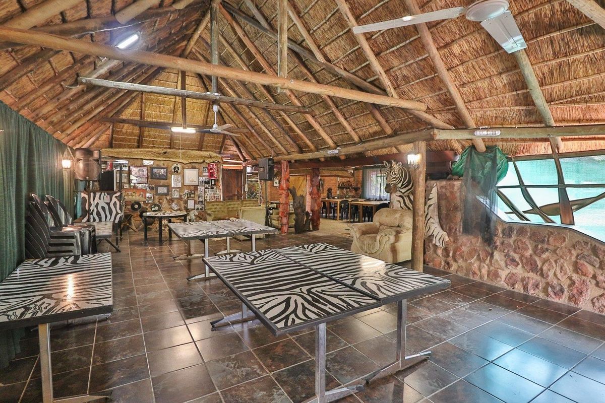 Spacious living area featuring a traditional thatched roof with exposed timber trusses, stone wall accents, and durable tiled flooring.