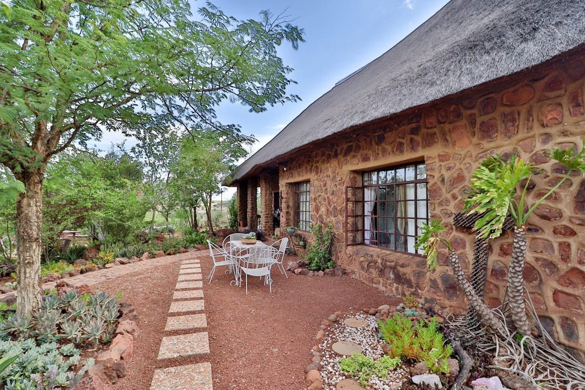 A charming farmhouse exterior featuring traditional stone masonry walls, a classic thatched roof, and steel casement windows, set within a landscaped garden area.