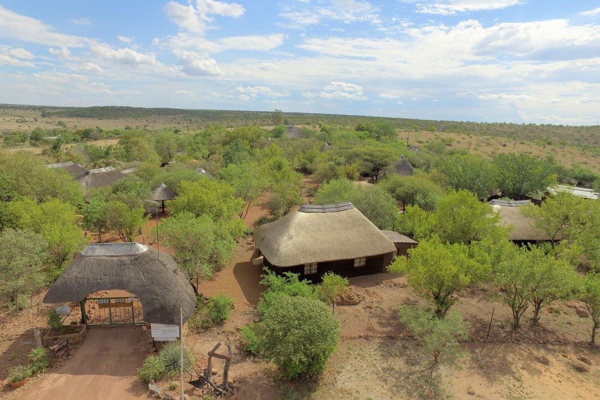 Aerial view of a rural farm property featuring multiple thatched-roof structures, mature trees, and a gated entrance set within a natural landscape.