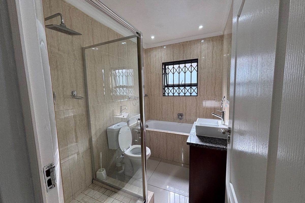 Modern bathroom featuring a glass-enclosed shower, built-in bathtub, vanity with countertop basin, and neutral wall tiling.
