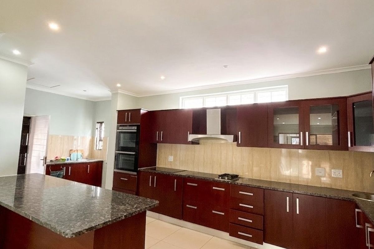 Spacious kitchen featuring dark wood cabinetry, granite countertops, a central island, and integrated appliances including a double wall oven and extractor fan.