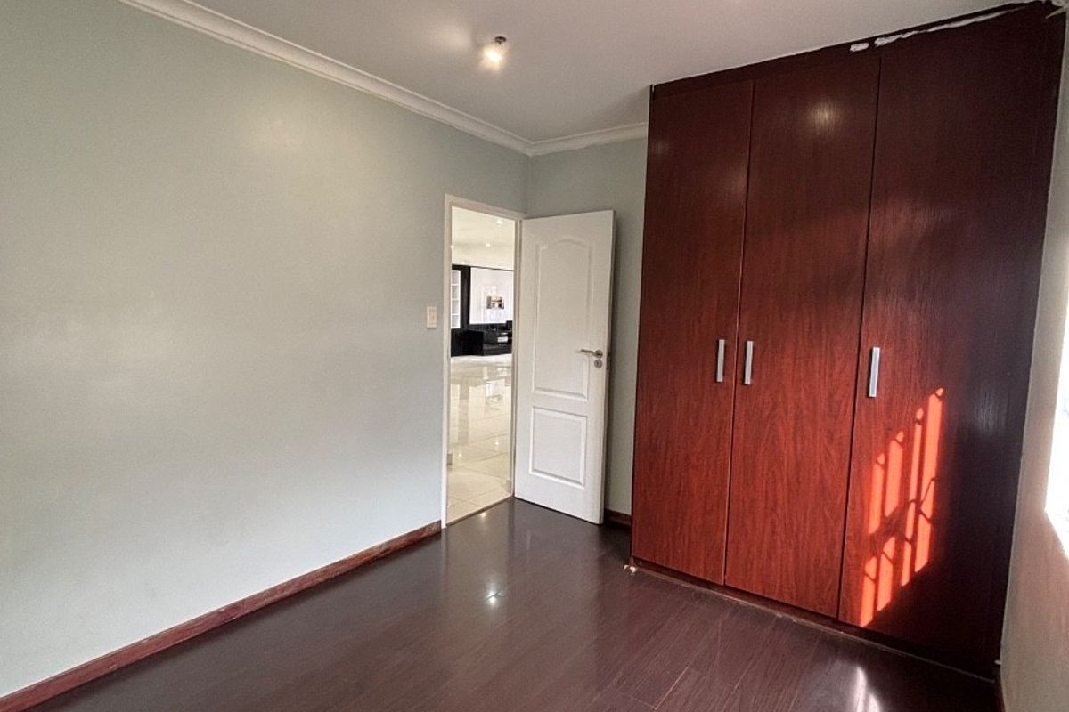 An empty bedroom featuring dark laminate flooring, built-in wooden wardrobes, and recessed ceiling lighting.