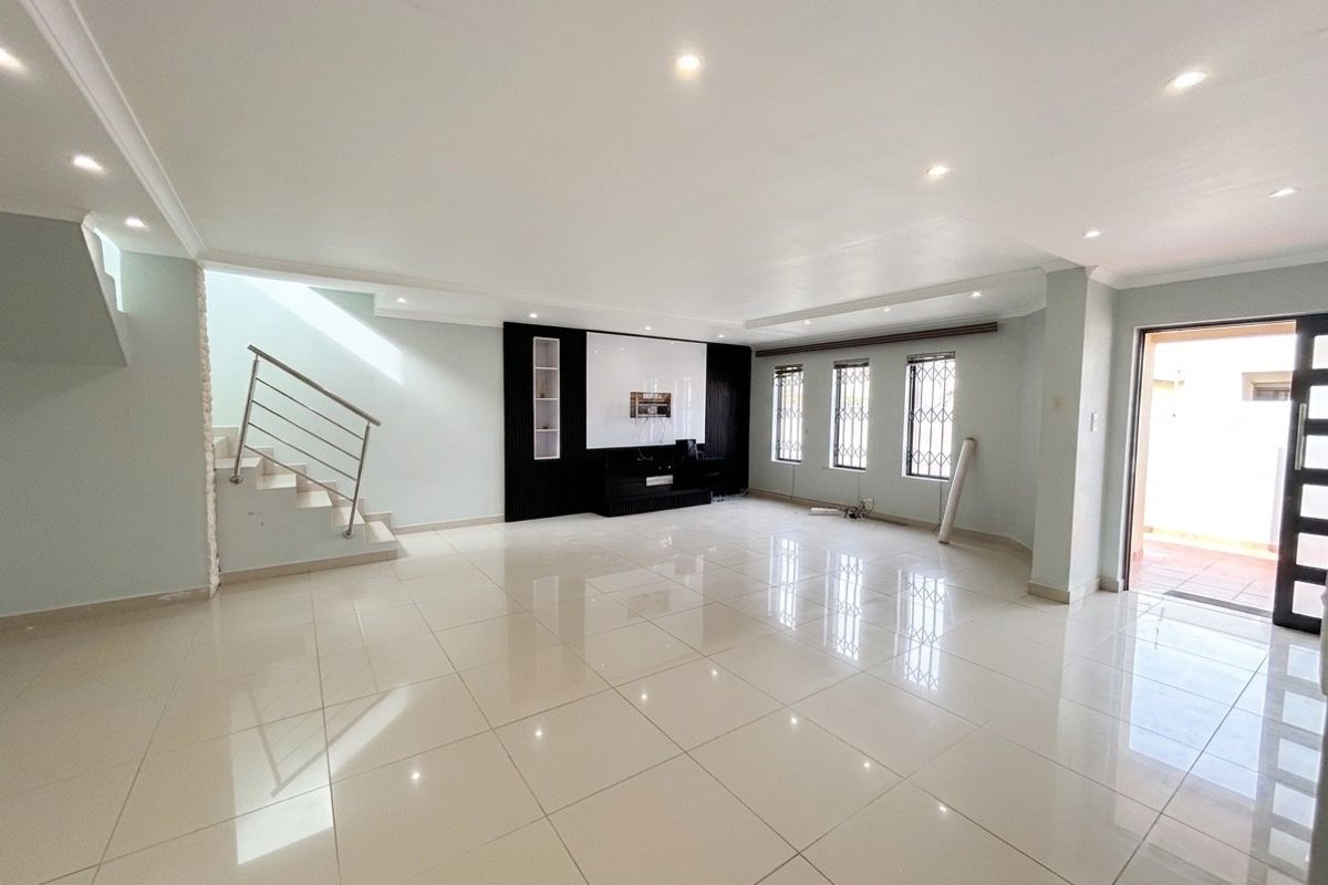 Spacious open-plan living area featuring polished tiled floors, a built-in media wall, recessed lighting, and a staircase with a modern metal balustrade.