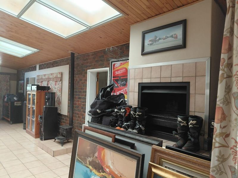 Living room featuring a tiled fireplace, wood-burning stove, exposed brick wall, and timber ceiling with integrated skylights.