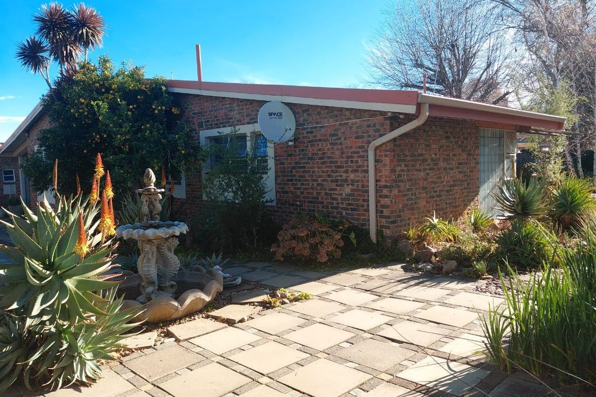 A rear exterior view of a brick house featuring a paved patio area, established garden landscaping, and guttering system.