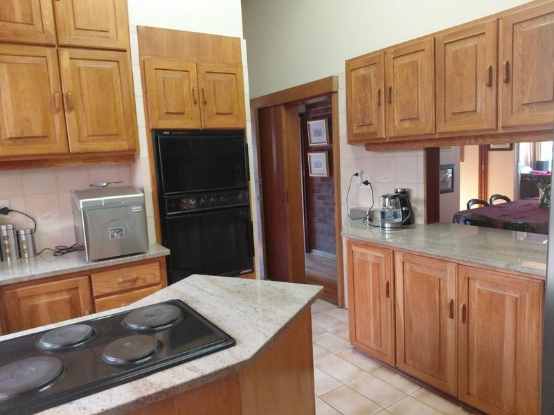 A functional kitchen featuring traditional wooden cabinetry, granite countertops, a built-in oven, and an electric hob with tiled flooring.