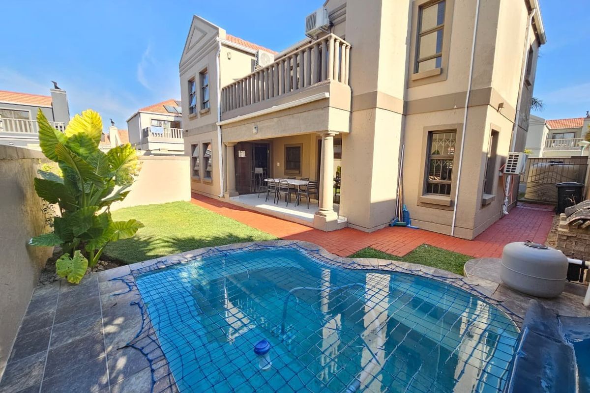 Rear exterior view featuring a swimming pool with safety net, a covered patio area, and an upper-level balcony on a two-story residential property.