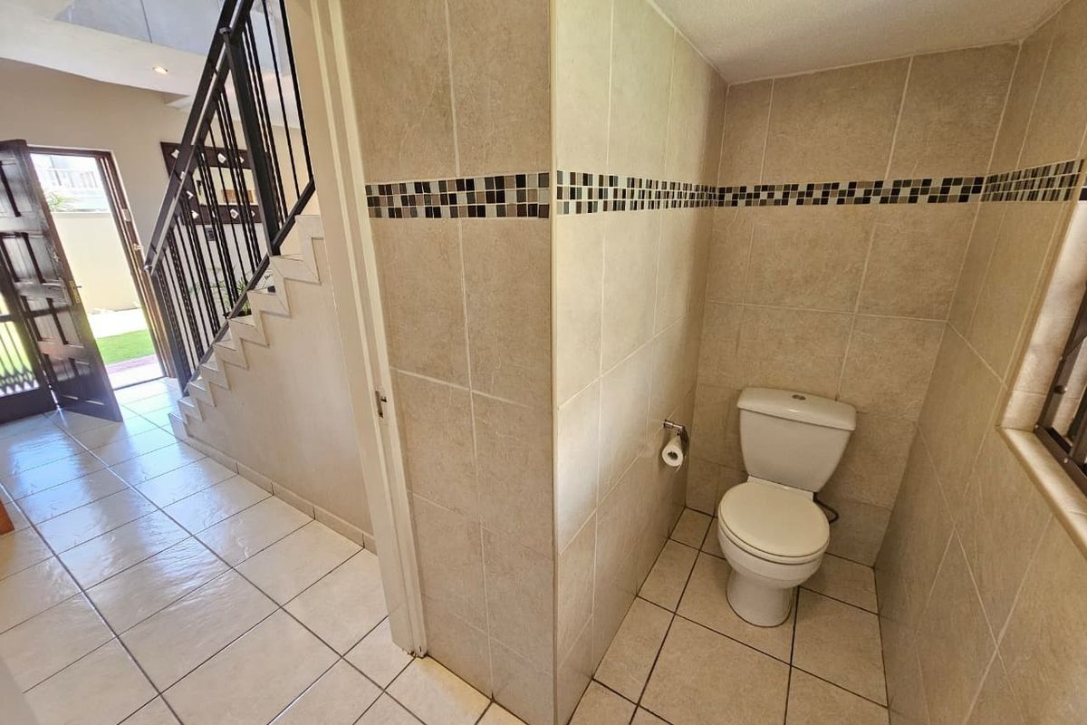 A compact guest bathroom featuring neutral ceramic tiling and a standard toilet, situated adjacent to an internal staircase.