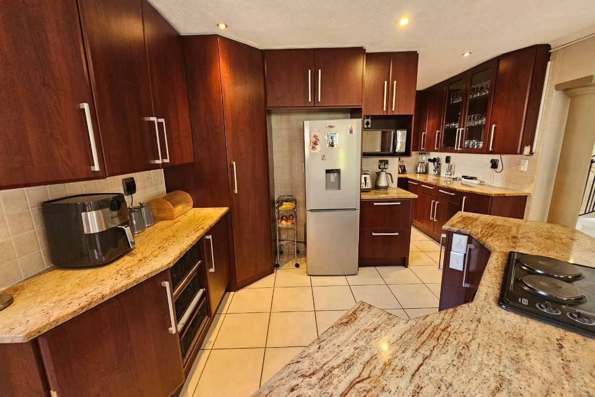 A functional kitchen featuring dark wood cabinetry, granite countertops, tiled backsplash, and ceramic flooring with integrated hob and ample storage space.