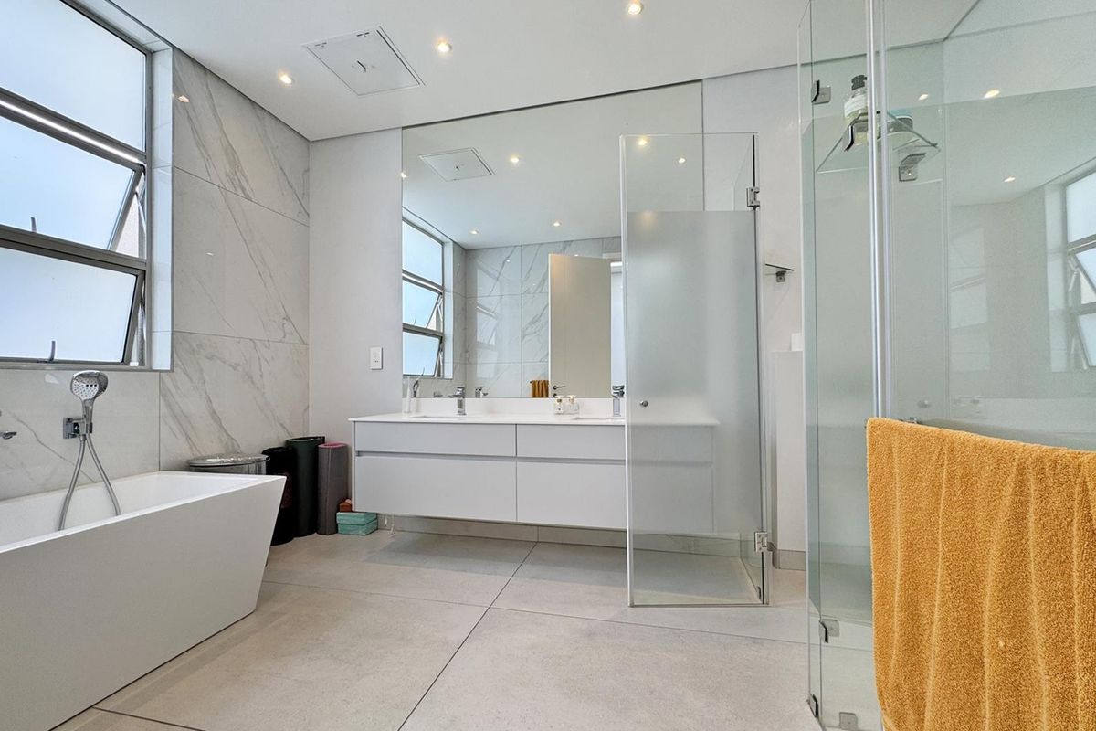 Modern bathroom featuring a sleek wall-mounted double vanity, a contemporary freestanding bathtub, and a spacious glass-enclosed shower with high-end marble-look wall tiling.