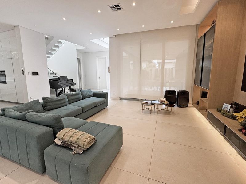 Spacious open-plan living area featuring large format floor tiles, recessed lighting, built-in cabinetry, and a modern staircase, creating a bright and contemporary atmosphere.