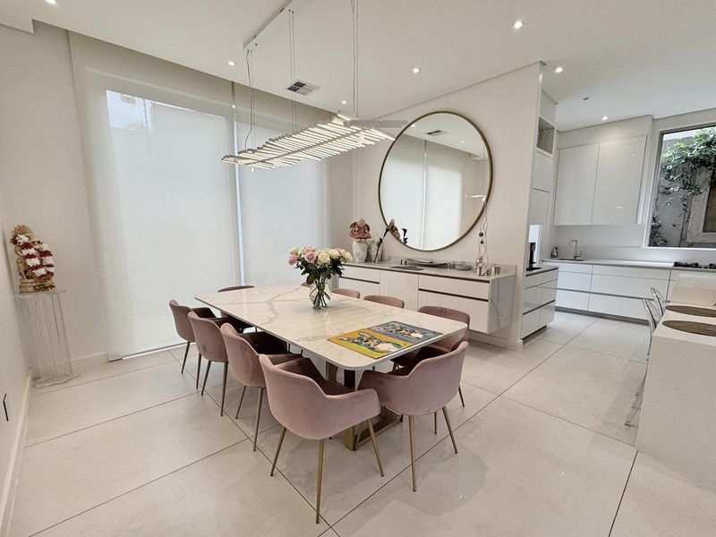 Modern open-plan dining and kitchen area featuring sleek white cabinetry, marble-topped surfaces, large-format floor tiles, and contemporary recessed and pendant lighting.