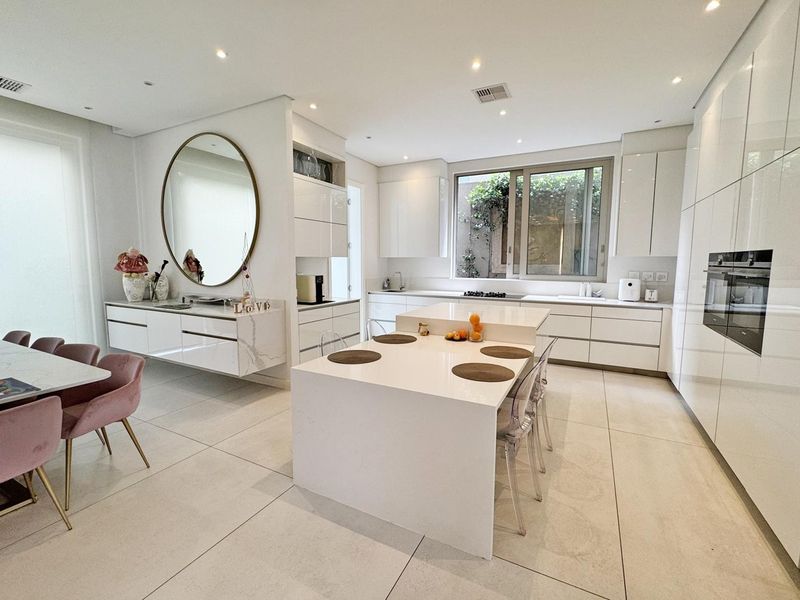 Modern open-plan kitchen featuring sleek white cabinetry, a central island with stone countertops, and high-quality finishes throughout.