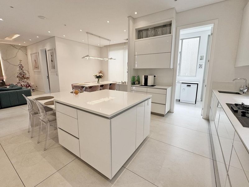 Modern open-plan kitchen featuring a central island, sleek white cabinetry, stone countertops, and integrated gas hob, seamlessly flowing into the dining and living areas.