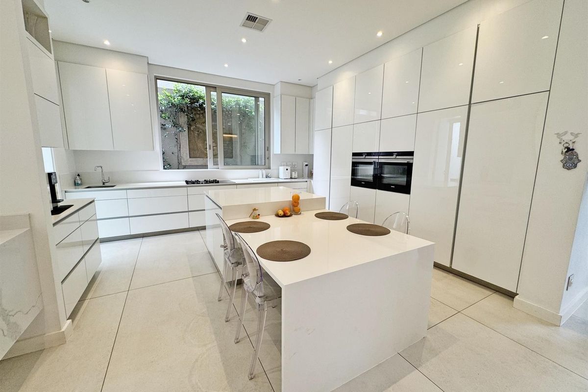 Modern, high-end kitchen featuring sleek white cabinetry, a large central island with integrated seating, double wall ovens, and premium stone countertops.