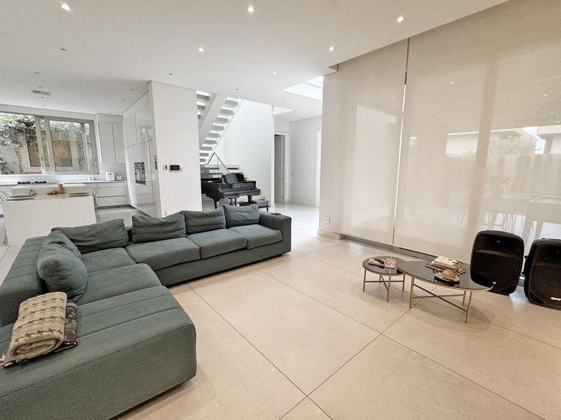 Spacious open-plan living area featuring large-format floor tiles, recessed lighting, a modern kitchen with integrated appliances, and a feature staircase.
