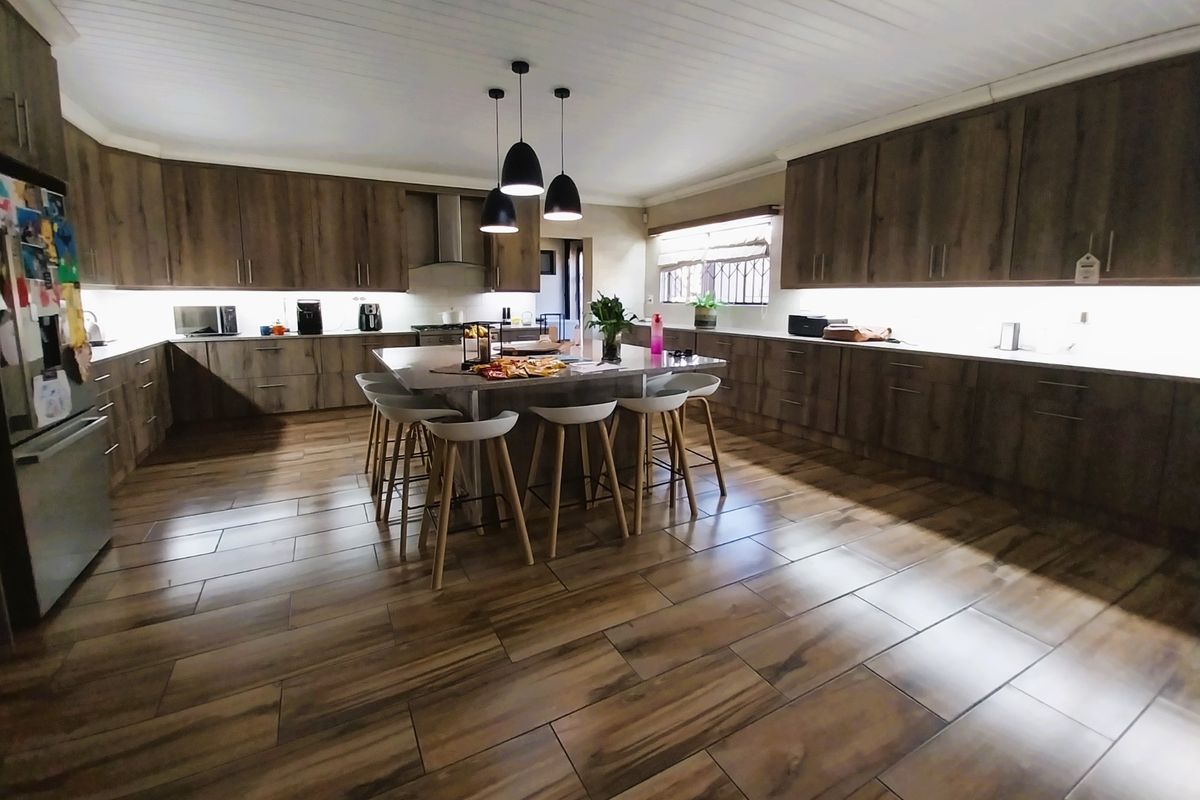 Spacious modern kitchen featuring extensive wood-finish cabinetry, a large central island with seating, under-cabinet lighting, and durable wood-look tiled flooring.