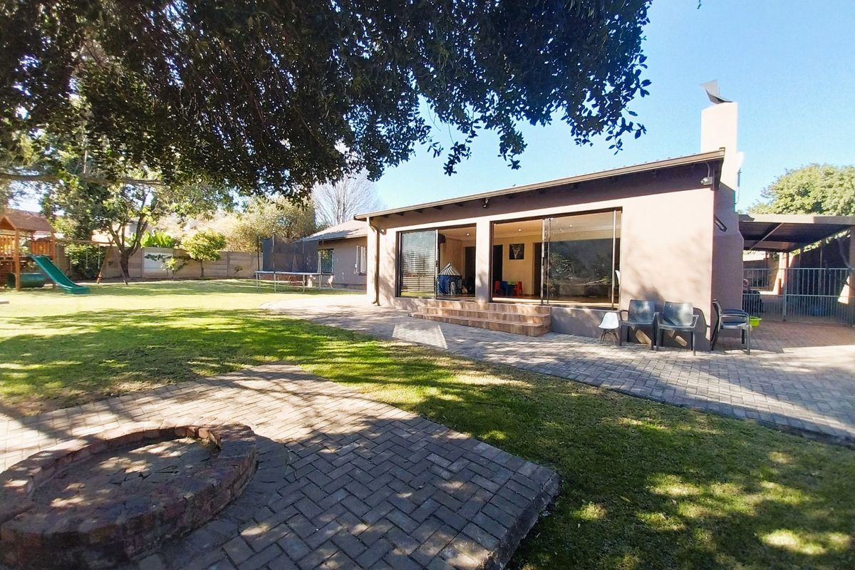 Rear view of the house featuring a spacious garden, brick-paved patio area, built-in fire pit, and large sliding doors leading into the living space.