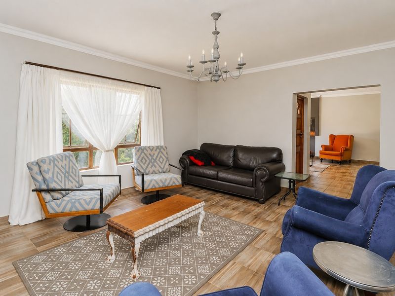 A spacious living room featuring tiled flooring, coved cornicing, and a central chandelier, offering a comfortable and well-maintained living space.