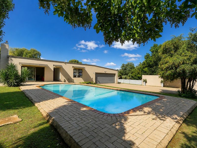 A well-maintained outdoor pool area featuring a paved deck, surrounding lawn, and direct access to the home's living space and garage.