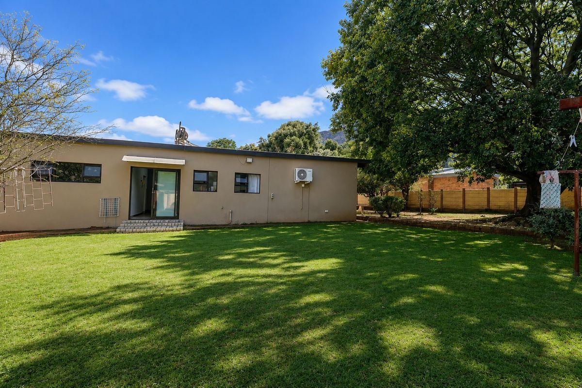 A view of the rear exterior of the house featuring a spacious lawn, established tree, and brick boundary wall.