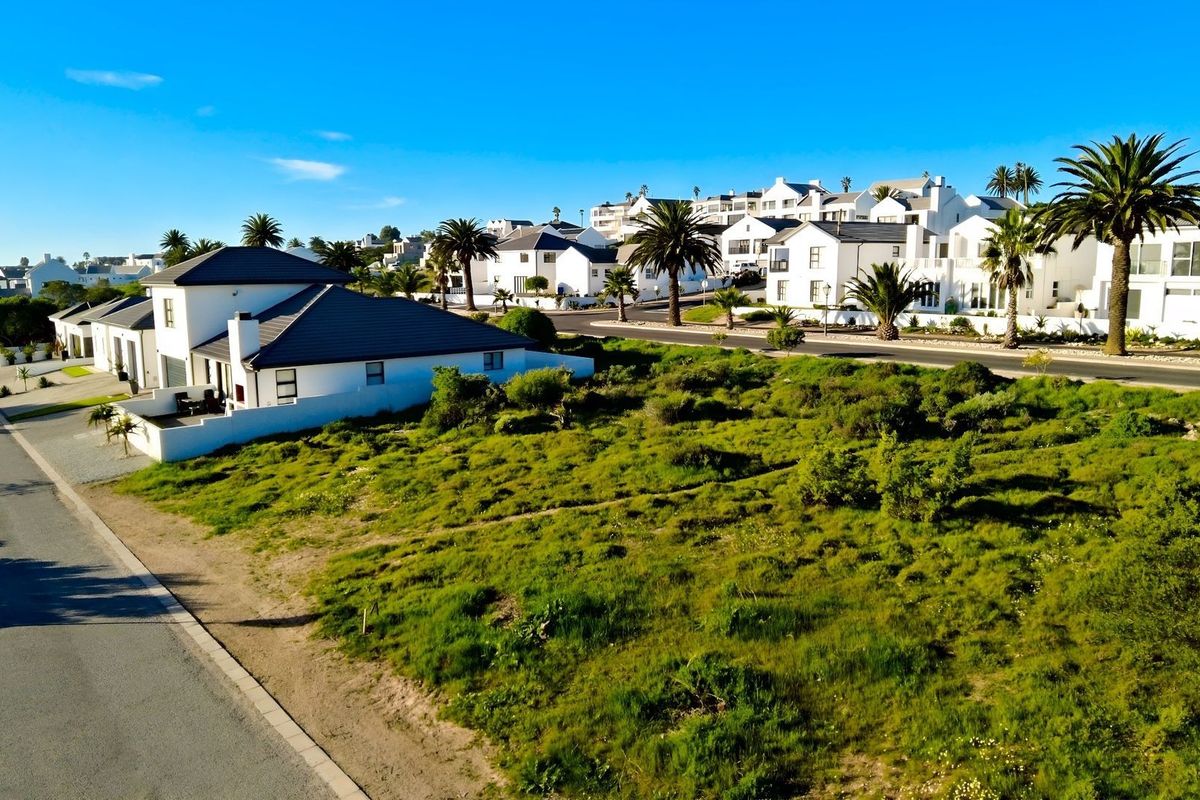 An aerial view of a vacant residential plot situated in a developed coastal estate, surrounded by established homes and paved street infrastructure.
