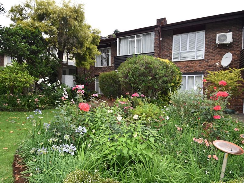 A rear view of the townhouse featuring a well-established garden with mature shrubs and flowers, set against a classic brick facade.