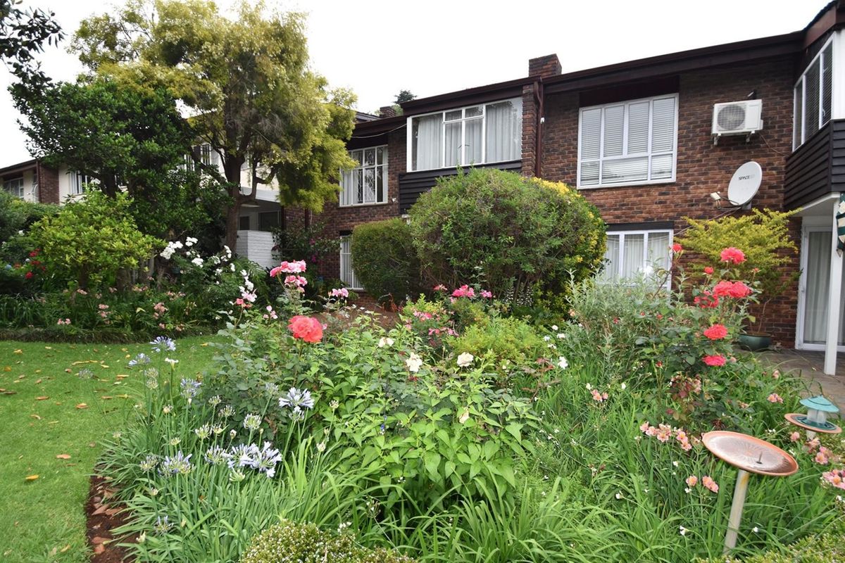 A rear view of the townhouse featuring a well-established garden with mature shrubs and flowers, set against a classic brick facade.