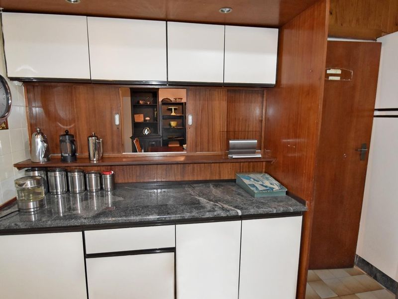 A dated kitchen area featuring wood-tone cabinetry, stone countertops, and a convenient sliding serving hatch connecting to the adjacent living space.