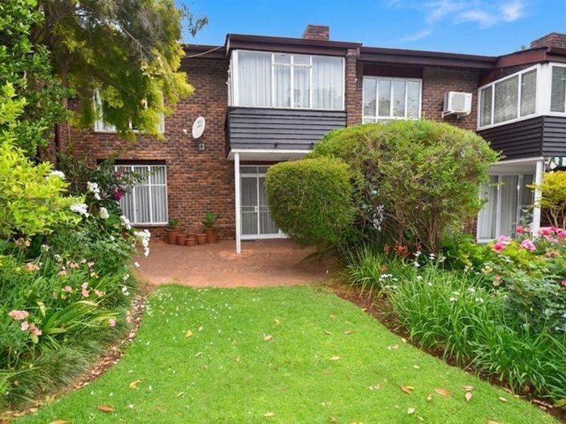 Rear view of the townhouse featuring a private paved patio, established garden, and lawn area with brick and timber facade detailing.