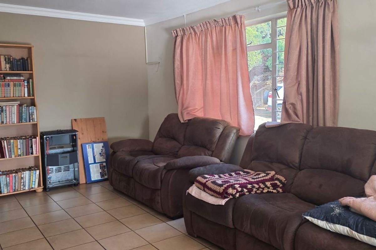 A living room featuring tiled flooring, coving, and a window with security bars, providing a functional and lived-in space.