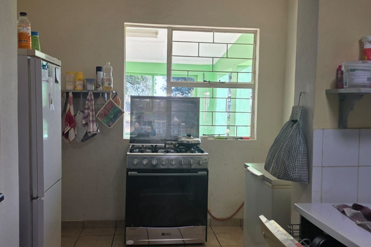A functional kitchen area featuring a gas stove, oven, tiled flooring, and wall-mounted shelving, with a window providing natural light and security bars.