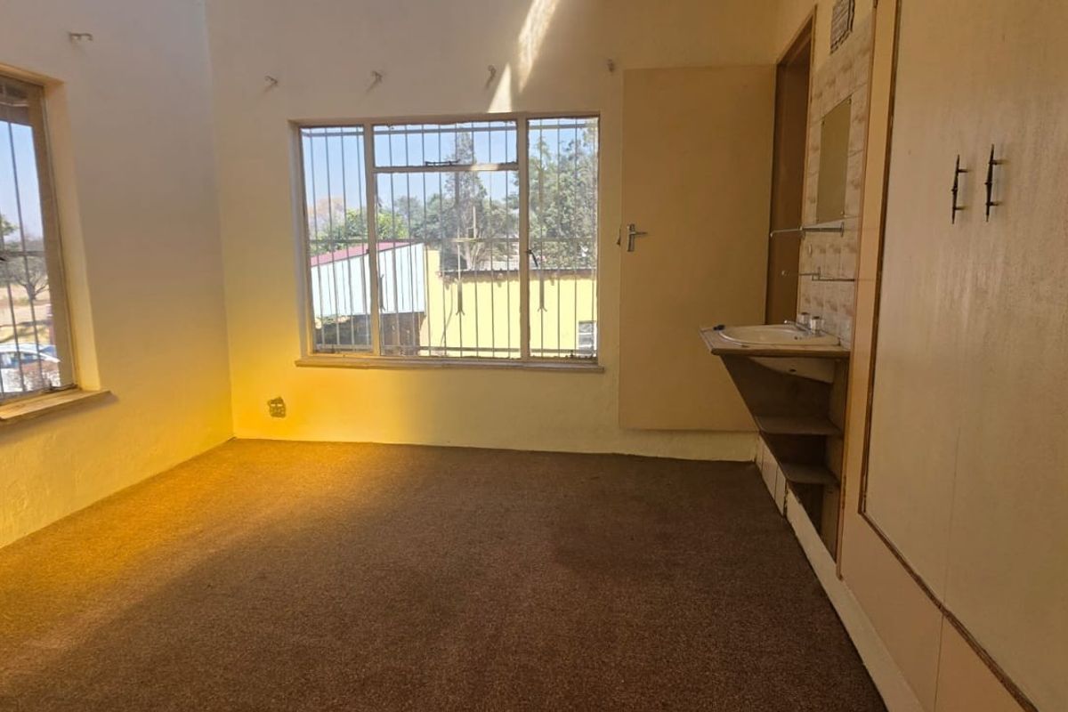 An empty bedroom featuring built-in cupboards, a wall-mounted basin, and security bars on the windows, offering a blank canvas for renovation.