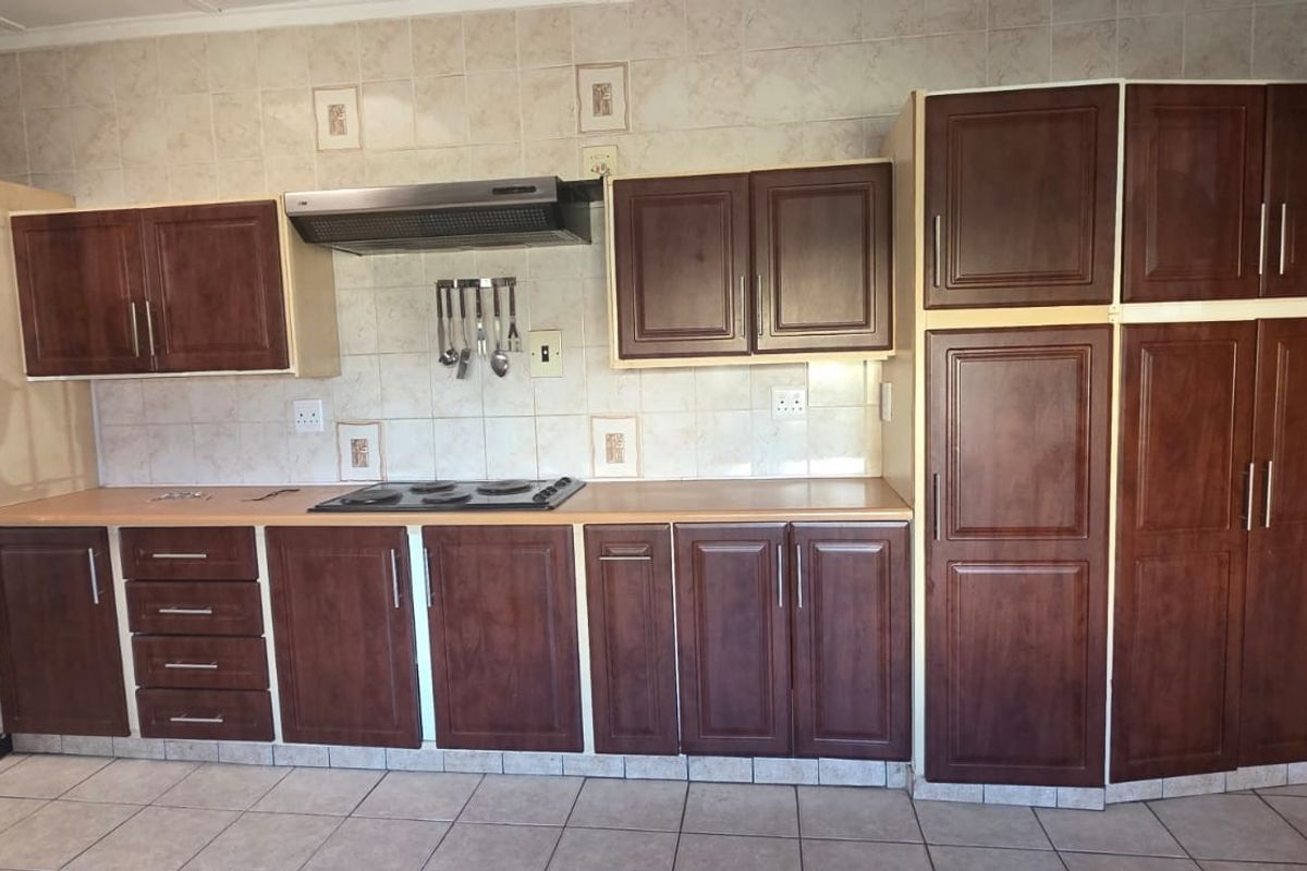 A functional kitchen featuring dark wood-finish cabinetry, laminate countertops, a built-in oven, and an electric hob with an extractor fan.