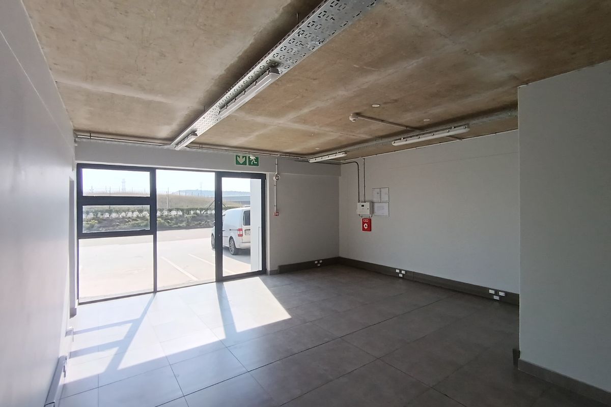 A clean, modern industrial utility space featuring exposed concrete ceilings, tiled flooring, and large glass doors providing ample natural light.