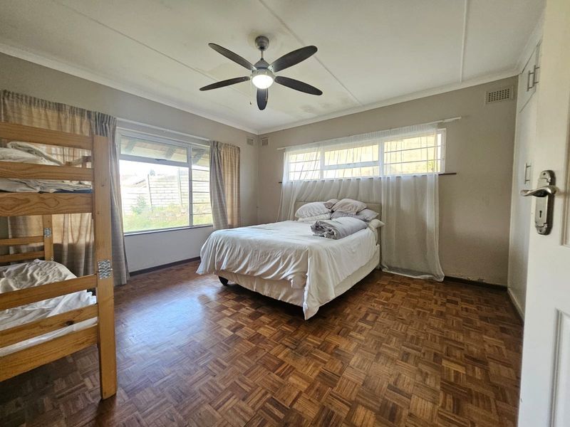 Spacious bedroom featuring classic parquet flooring, a ceiling fan, and built-in storage cupboards with large windows providing natural light.