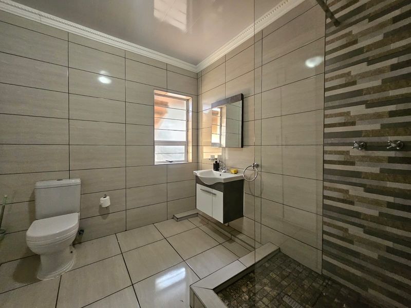 Modern bathroom featuring floor-to-ceiling neutral tiling, a walk-in shower with glass screen, and a contemporary wall-mounted vanity unit.
