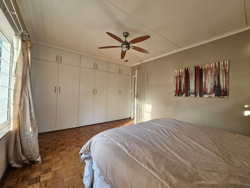 A well-maintained bedroom featuring classic parquet flooring, extensive built-in cupboard storage, and a ceiling fan, offering a clean and functional living space.