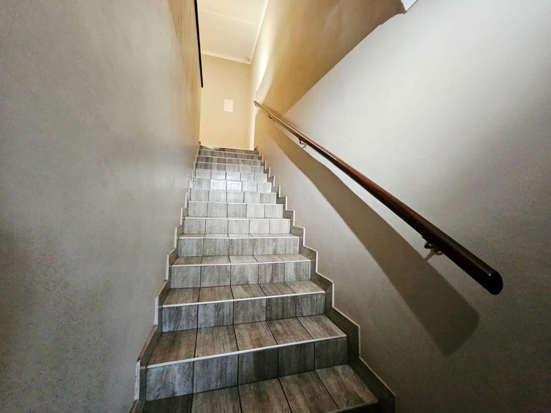 A clean, tiled staircase featuring a sturdy wooden handrail leading to an upper level.