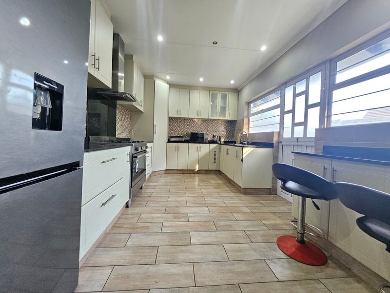 Modern kitchen featuring ample built-in cabinetry, granite countertops, a gas stove with extractor, and tiled flooring, offering a functional and well-lit workspace.